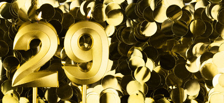 Golden number twenty-nine candle on shiny yellow confetti background. Festive backdrop for twenty-ninth birthday, anniversary or celebration. Bright greeting card with space for text.の写真素材