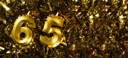 Golden candles number 65 on gold tinsel background. Celebration sixty-fifth birthday. Concept of celebrating birthday and anniversary.の写真素材