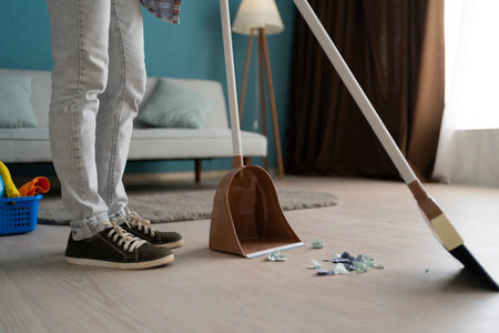 Unrecognizable woman sweeping floor using broom and dustpan doing house cleaning in living roomの写真素材