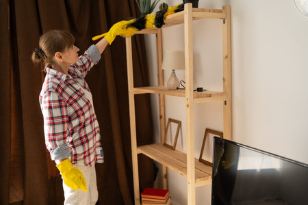 Spring cleaning concept. Housewife cleaning dust from shelf using duster. woman sweeping bookshelfの写真素材