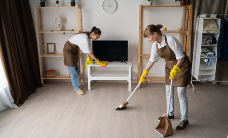 Two female janitors cleaning home wiping dust and sweeping in the living room. Concept of cleaning...