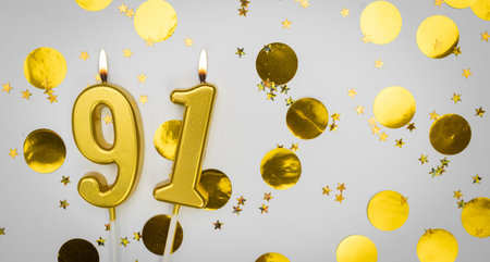 Number 91 golden celebration birthday candle on white with confetti background. Ninety-one years...