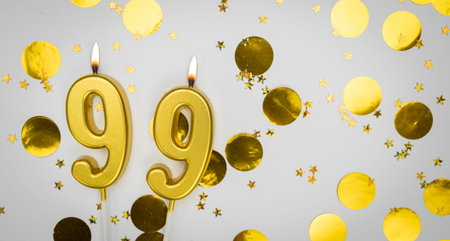 Number 99 golden celebration birthday candle on white with confetti background. Ninety-nine years birthday. Concept of celebrating birthday, anniversary.の写真素材