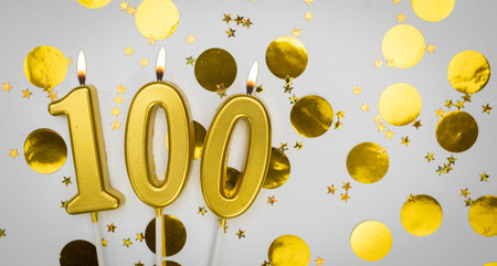 Number 100 golden celebration birthday candle on white with confetti background. One hundred years...