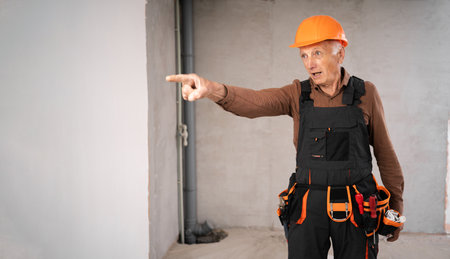 Elderly mature male builder in safety helmet angry finger pointing at away with negative emotions. profession, construction and building concept.の写真素材