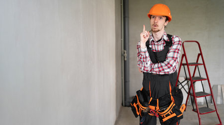 Builder man in safety hardhat making idea gesture with finger in renovation roomの写真素材