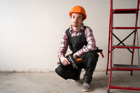 Portrait of Construction Worker Holding Drill While Sitting Near Ladder at Home Renovation Siteの写真素材