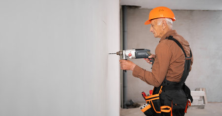 Professional builder or handyman in hardhat using a drill drilling hole in the wallの写真素材