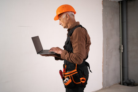 professional male builder showing construction on new house. civil engineer in safety helmet using laptop computerの写真素材