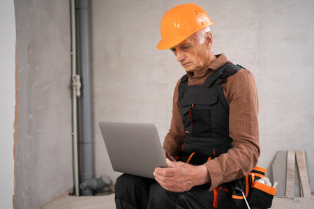 Elderly builder or civil engineer with a laptop working indoors new house. Architect or engineer are designing buildings.の写真素材