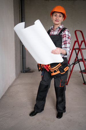 professional foreman at work. Middle-aged female builder with plan of rooms new apartment, civil engineer working in home renovationの写真素材
