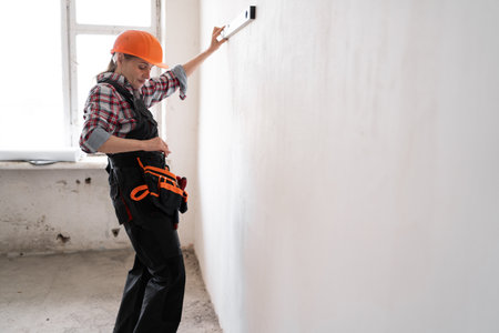 Female construction worker or builder wearing protective helmet uses spirit level for measurement wall during renovation or construction workの写真素材