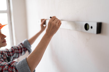 Female builder or construction worker measures wall in new house with a spirit level.の写真素材