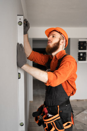 construction foreman using spirit level on concrete wall. Repairman wearing blue coveralls at...