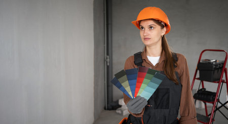 female painter in workwear holding color palette samples with thoughtful expression while making...