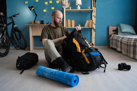 packing for a trip at home. Traveler packing a backpack and accessories for a mountain hike while sitting on the floor in a room at homeの写真素材
