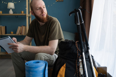 Thoughtful bearded man writing a list of things for a hike looking awayの写真素材