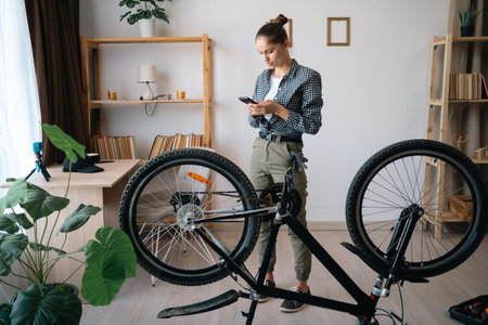 Young woman using smartphone following internet tutorial videos learning to fix damaged bike.