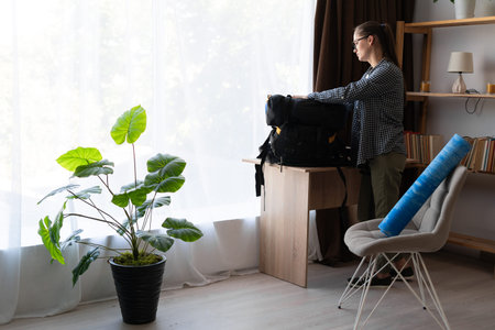 female hiker preparing for mountain hike packing backpack and equipment in living room of her apartmentの写真素材