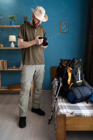 Young bearded man traveler prepare for hiking vacation holding camera at home. backpacker travel