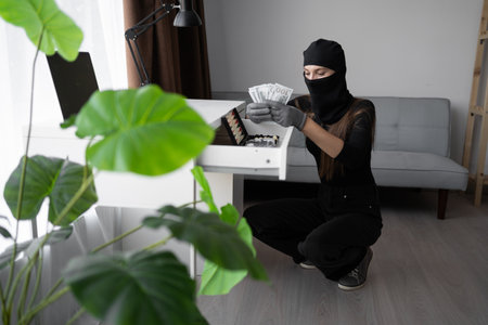 Theft, burglary and crime concept. Female thief in black balaclava stealing money from house, crime sceneの写真素材