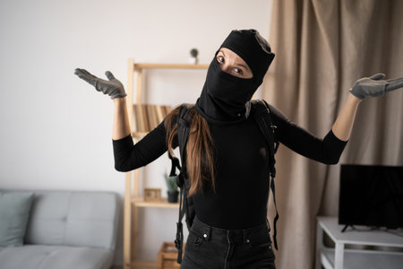 A person in a black balaclava making a gesture raising her hands up looking at the camera puzzledの写真素材