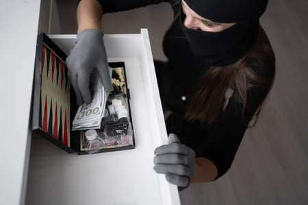 Burglar, robber or thief breaks home. Woman wearing black balaclava stealing money cash from house...