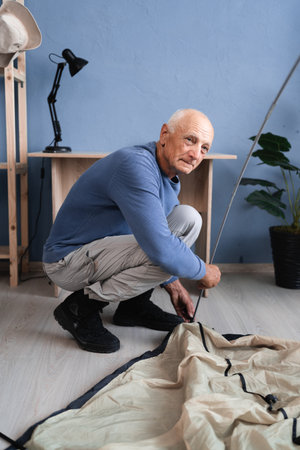 A pensioner setting up a camping tent prepares for a hike and checks equipment at home.の写真素材