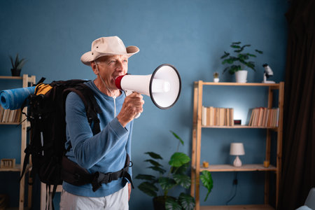 Retired traveler with backpack screaming in megaphone at home. sincere emotions lifestyle. Tourist makes active healthy lifestyle. Hiking, travel and tripの写真素材