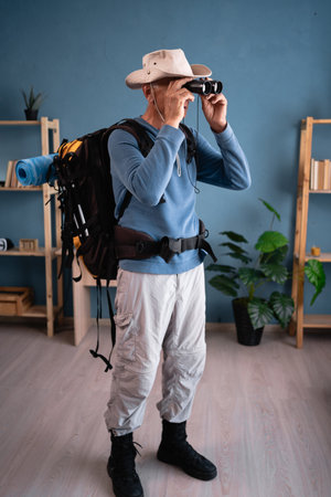 Retired traveler with backpack with binocular standing at home. Tourist makes active healthy lifestyle. Hiking, travel and tripの写真素材