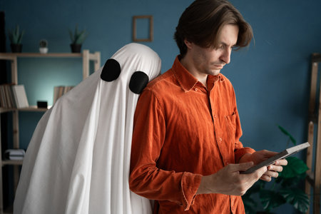 Concept of afterlife and memory for lost love. Depressed sad widower looking old photo while female ghost standing near in the living room. Dead wife. Life and deathの写真素材