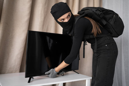 Female thief stealing tv from apartment. Criminal, house crime and breaking. robbery and burglary on propertyの写真素材