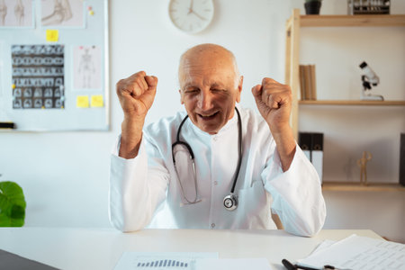 mature doctor with stethoscope works on a laptop looking at camera. Senior therapist making video call, practitioner gp consulting patient onlineの写真素材