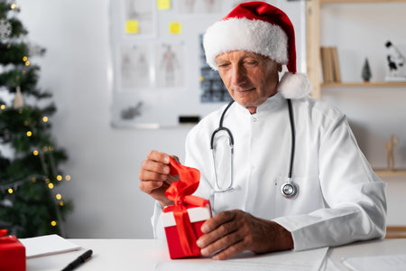 Senior Elderly Doctor in Santa hat with gift box on the shift in the hospital on Christmas Eveの写真素材