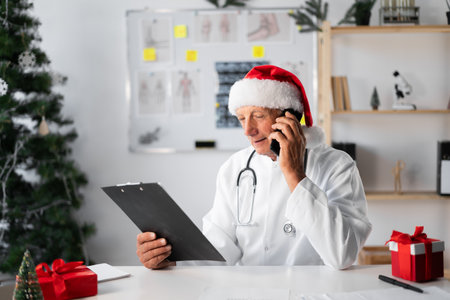 Senior Elderly Doctor in Santa hat with clipboard calling on phone at hospital on the shift on Christmas Eve. medicine, technologyの写真素材