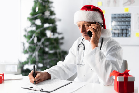 Senior Elderly Doctor in Santa hat consulting patient in phone conversation professional healthcare on the shift in the hospital on Christmas Eve. medicine, holiday, technology, and healthcareの写真素材