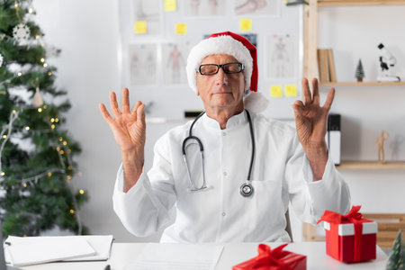 Senior elderly Doctor in Santa hat on the shift on christmas eve making breathing, working out, meditation, wellnessの写真素材