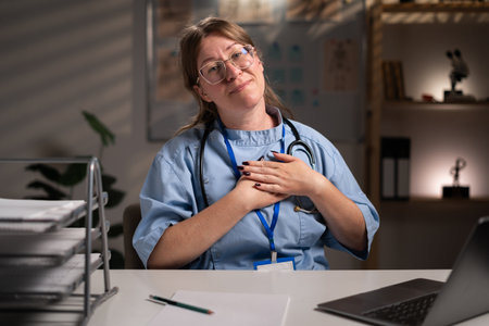 grateful thankful nurse working overtime on night put folded hands on heart in hospital office. Health care and medicine serviceの写真素材