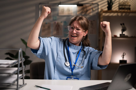Winning success nurse working overtime on night celebrating being a winner in hospital office. Victory, delight concept. Health care and medicine serviceの写真素材