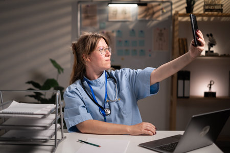 physician nurse using smartphone taking selfie working over hours in hospital office on night shift. Medicine and Health care serviceの写真素材
