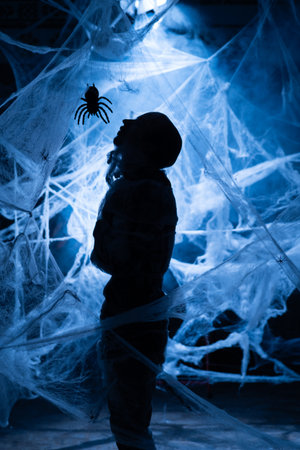 Man in spiders web with spider insect on black background. Blue light for halloweenの写真素材