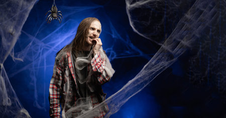 Creepy scary zombie man with ugly makeup nervous biting his nails in stress standing on spooky...