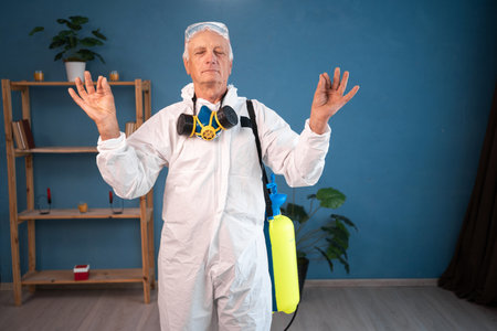 portrait of Elderly pest control worker in meditation yoga pose inside house. Exterminator in protective suit holding spray bottleの写真素材