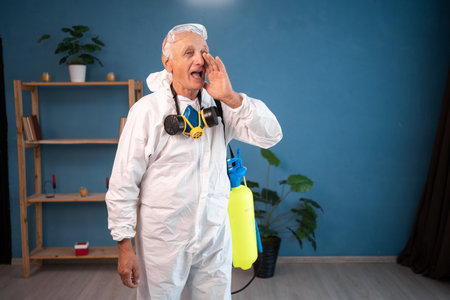 portrait of elderly pest control worker whispers inside infested house. Exterminator in protective suit holding spray bottle with insecticide for homeの写真素材