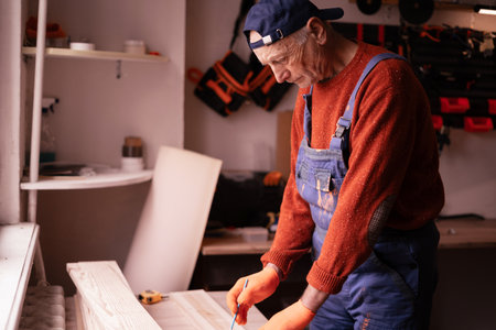 Profession, Small business and hobby concept. Senior elderly carpenter measuring wooden board using tools for work in workshop. Woodworker in carpenter shop. copy spaceの写真素材