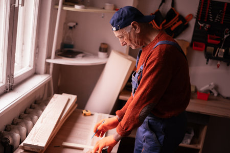 Profession, Small business and hobby concept. Senior elderly carpenter measuring wooden board using tools for work in workshop. Woodworker in carpenter shop. copy spaceの写真素材
