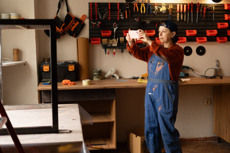 Young professional mechanic or craftsman woman in blue overalls take photo on mobile phone fix work...