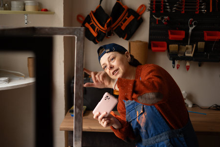 Young professional mechanic or craftsman woman in blue overalls take photo on mobile phone fix work...