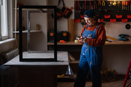 Portrait of mechanic or handyman woman standing with smartphone, having a break scrolling social...