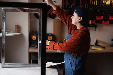 Handyman measuring metal legs in workshop with tape measure during furniture assembly. Concept of...
